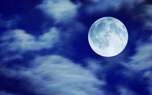 A full Moon reveals itself through clouds.