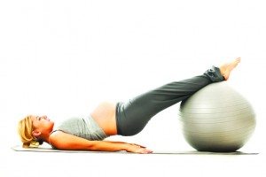 Beautiful blonde pregnant woman exercising with a fitness ball.